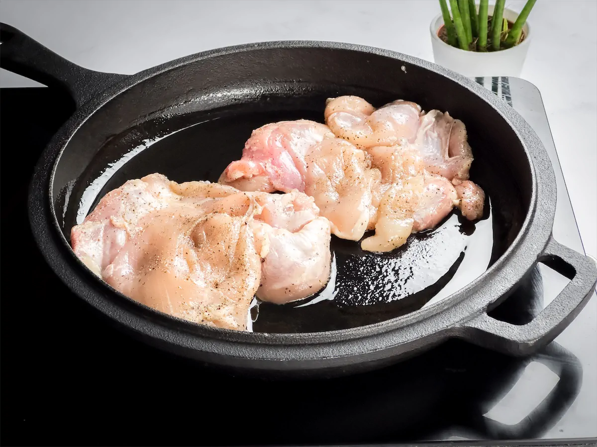 Cooking the boneless, skinless chicken thighs with olive oil in a cast iron skillet.