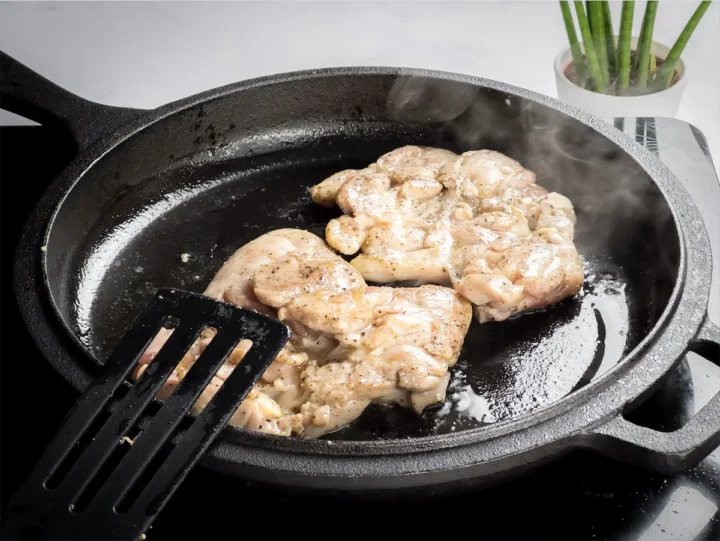 Skinless boneless chicken thigh cooking in a cast iron skillet.
