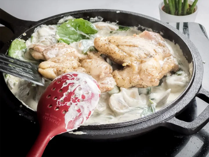 Adding cooked chicken thighs to the cast iron skillet with creamy white sauce.