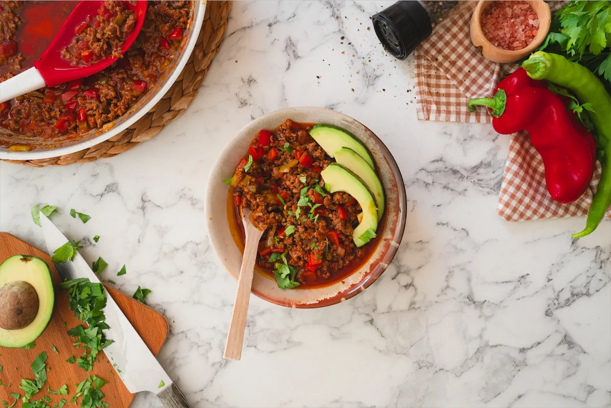 A serving of keto chili con carne in a bowl, topped with avocado slices.