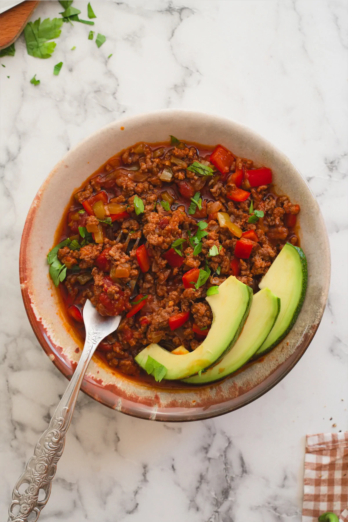Homemade keto chili con carne served in a bowl with avocado slices and a spoon.