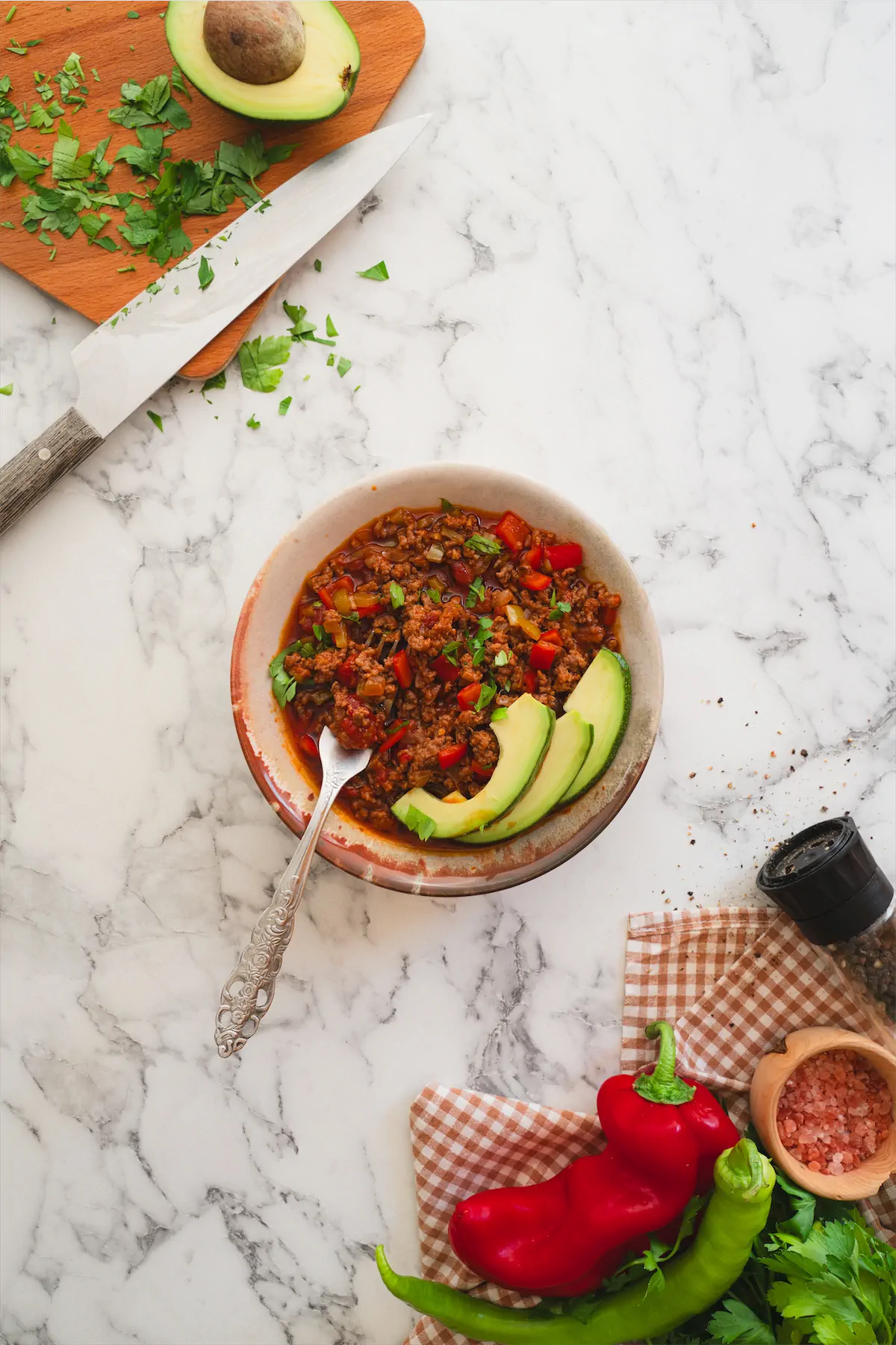 Keto chili con carne presented in a bowl with avocado slices and a spoon.