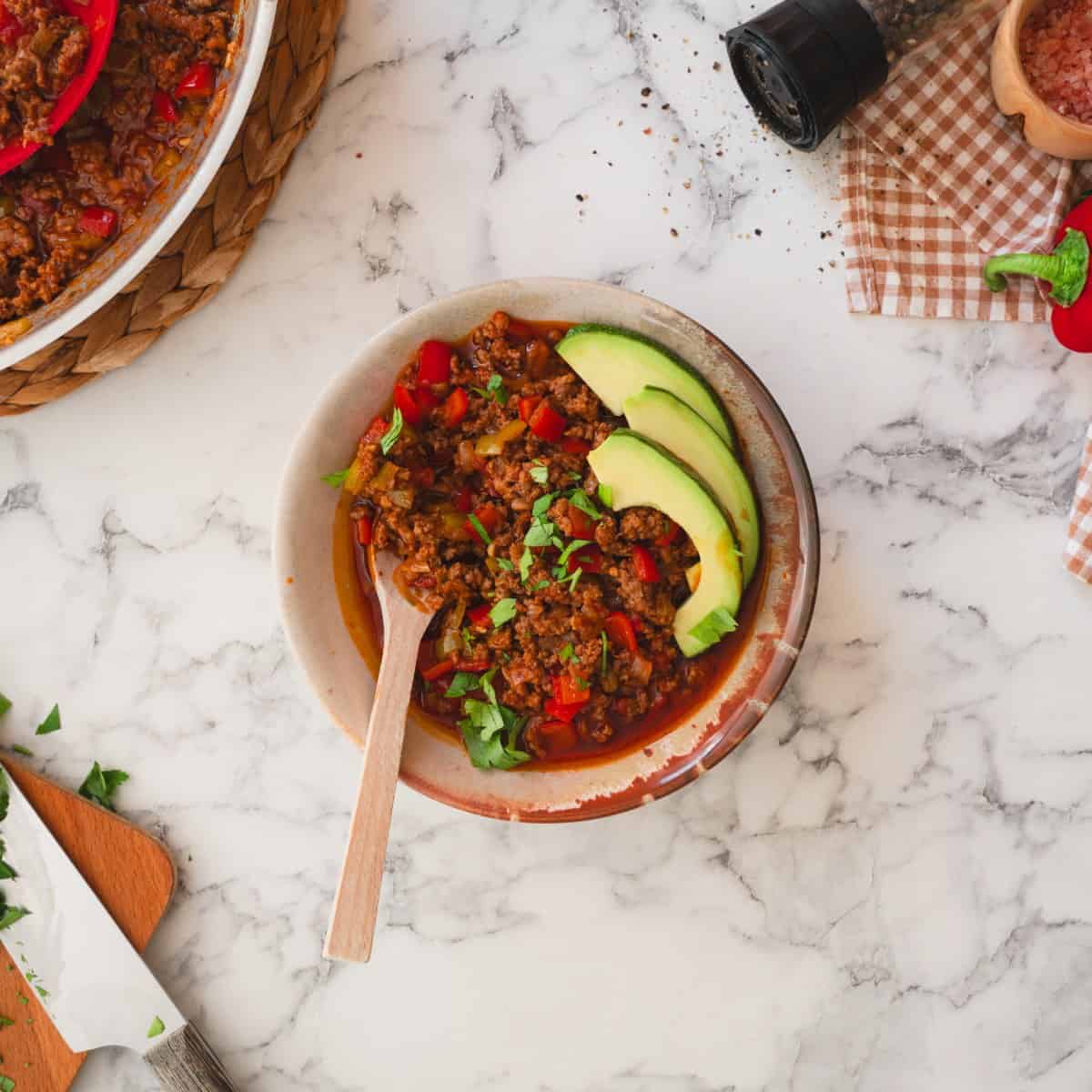 Keto chili con carne served with avocado slices in a bowl with a spoon.