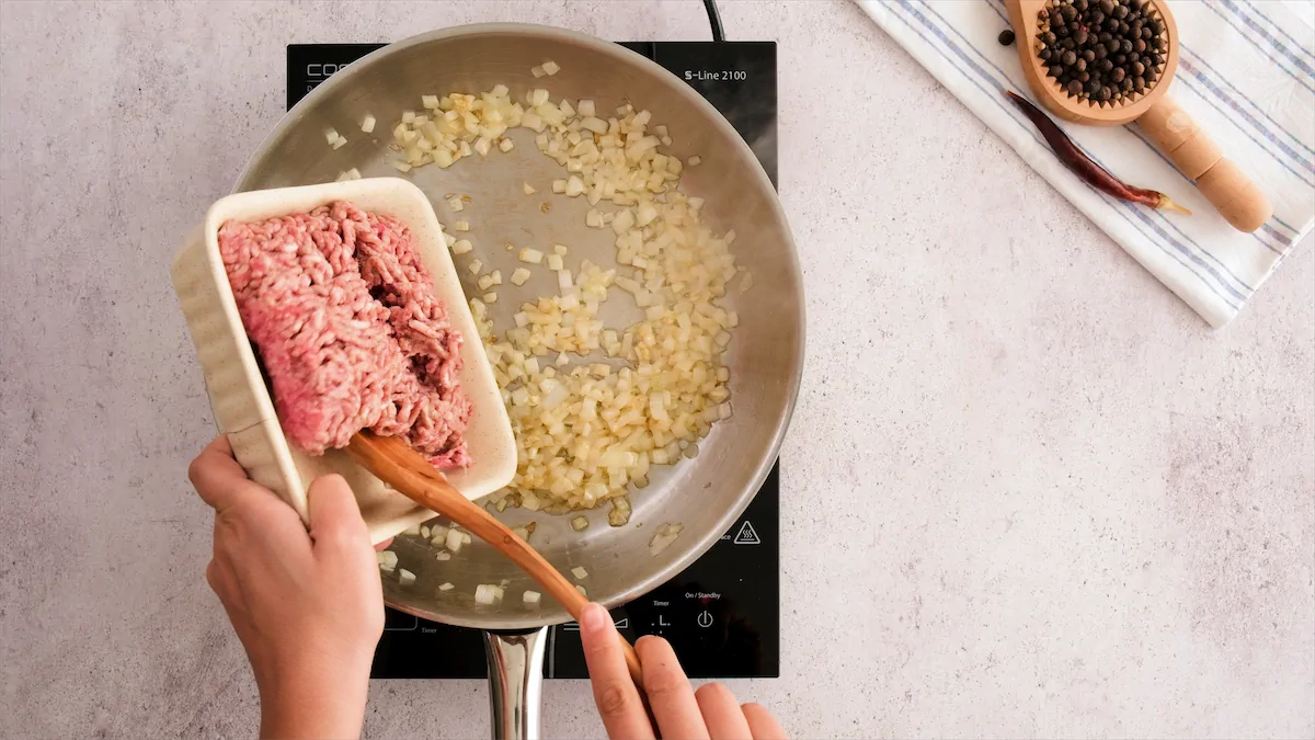 Adding ground beef to the stainless steel skillet with aromatics.