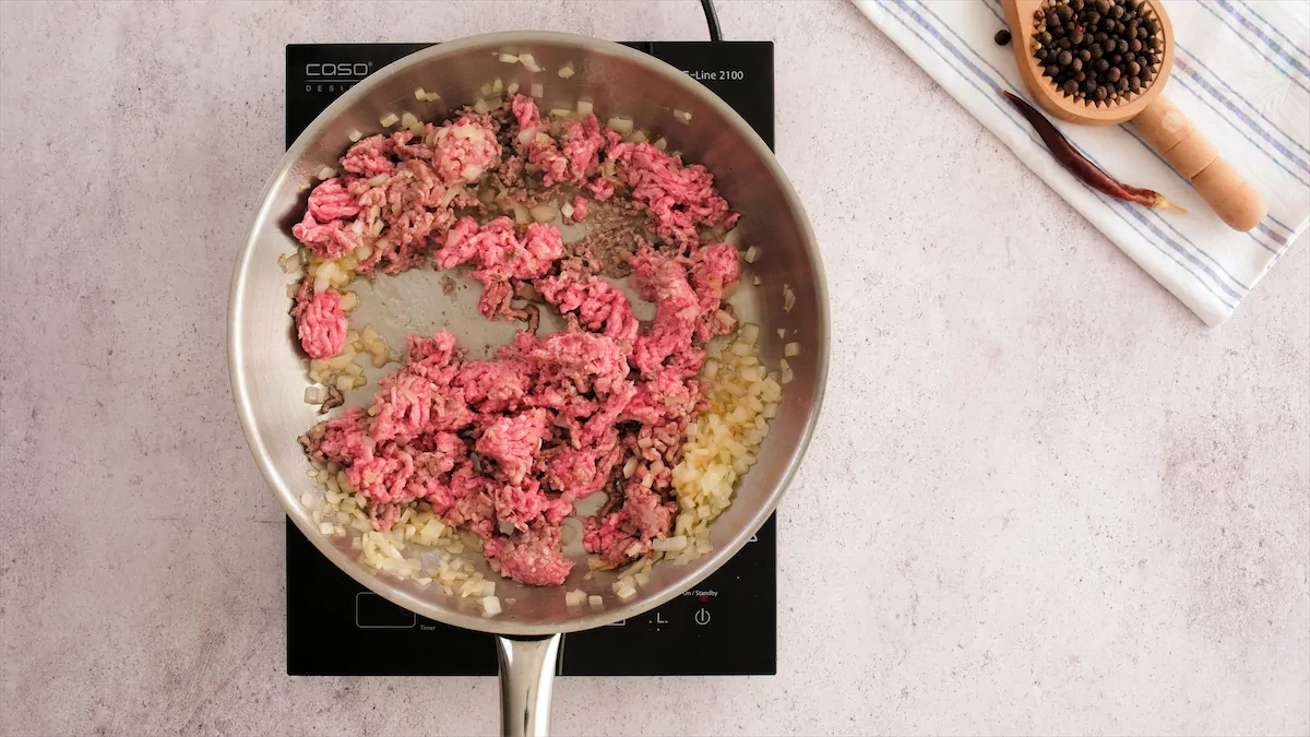 Cooking beef with aromatics in a stainless steel skillet.