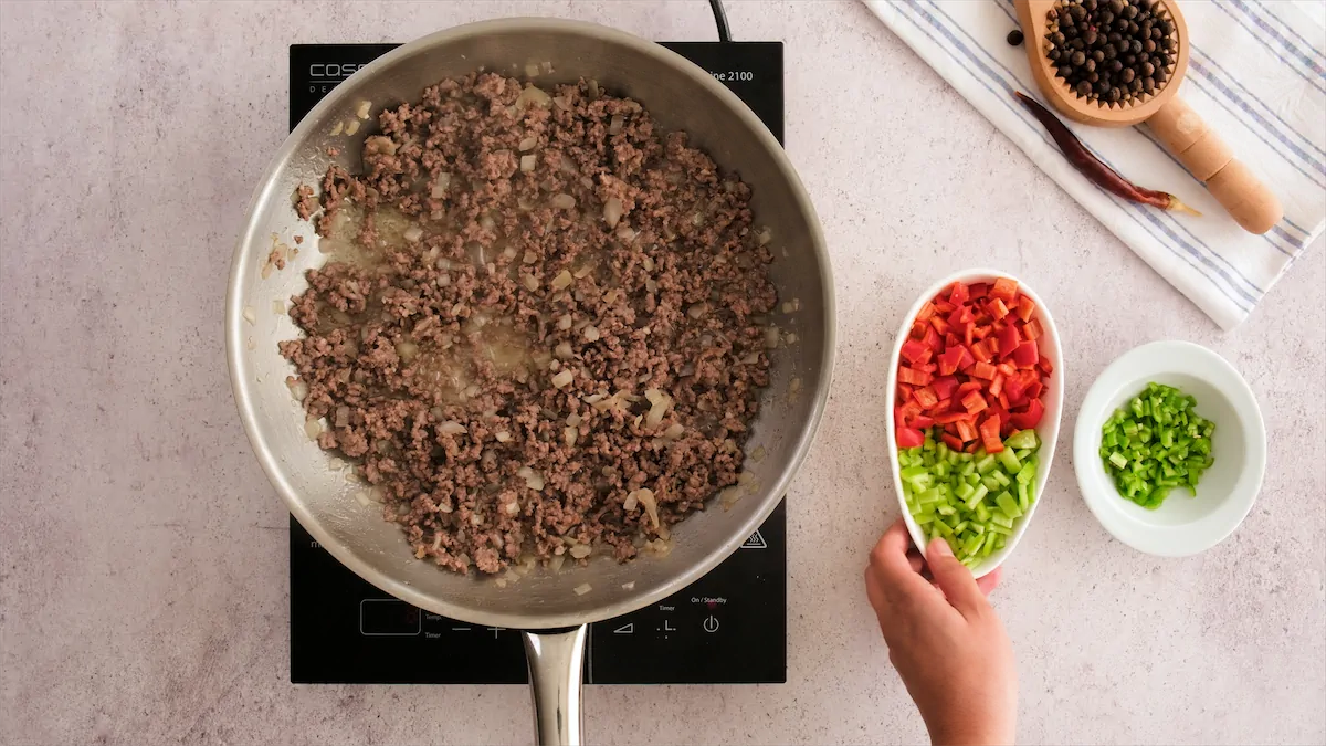 Cooking beef with aromatics in a stainless steel skillet, alongside diced red and green bell peppers and chopped jalapeño.