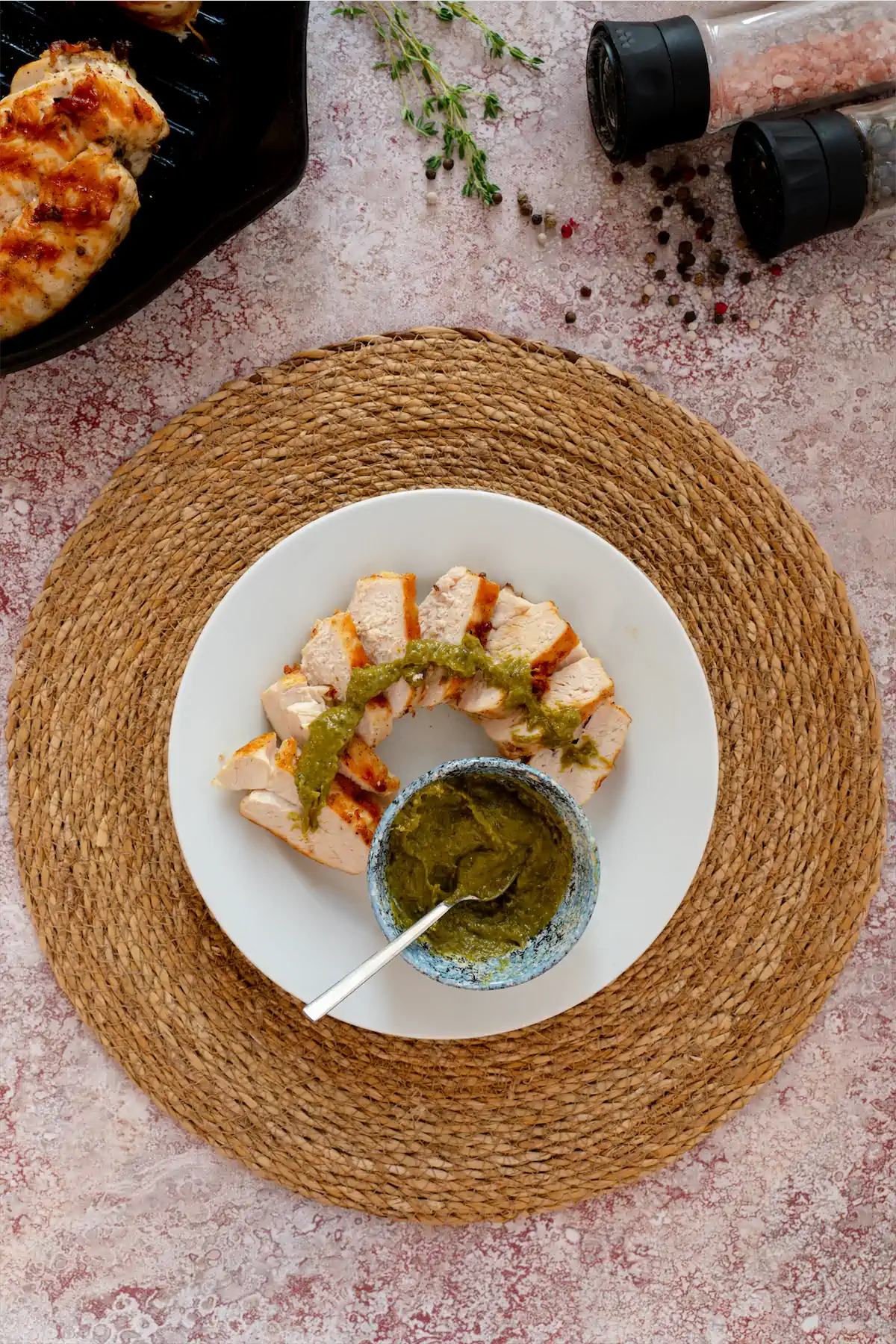 Keto grilled chicken slices drizzled with pesto sauce from the bowl on the same plate.