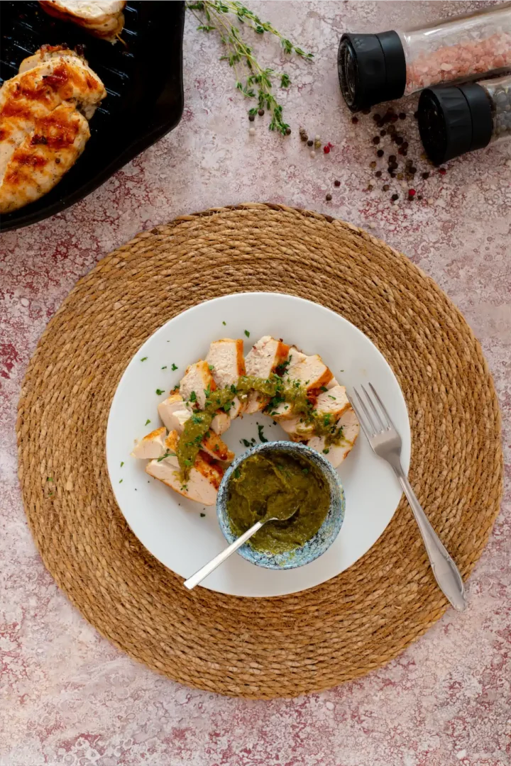 Keto grilled chicken slices with pesto sauce on a plate, and a bowl of pesto sauce on the side.