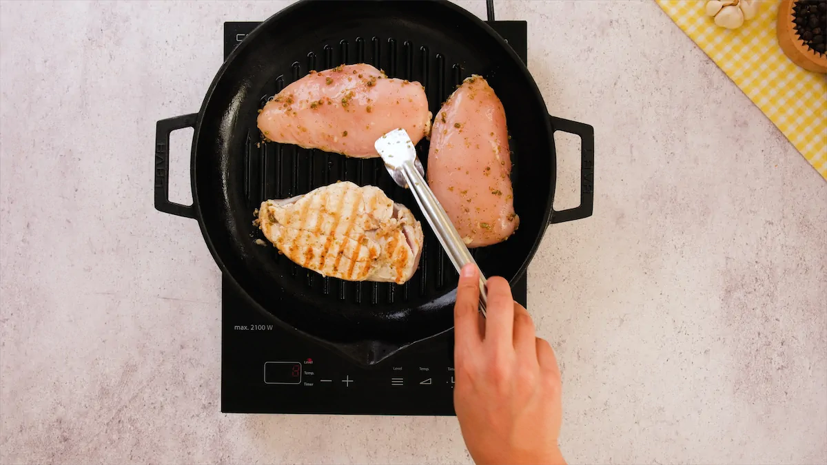 Flipping the chicken breast with a stainless steel tongs and the flipped chicken has golden grill marks.