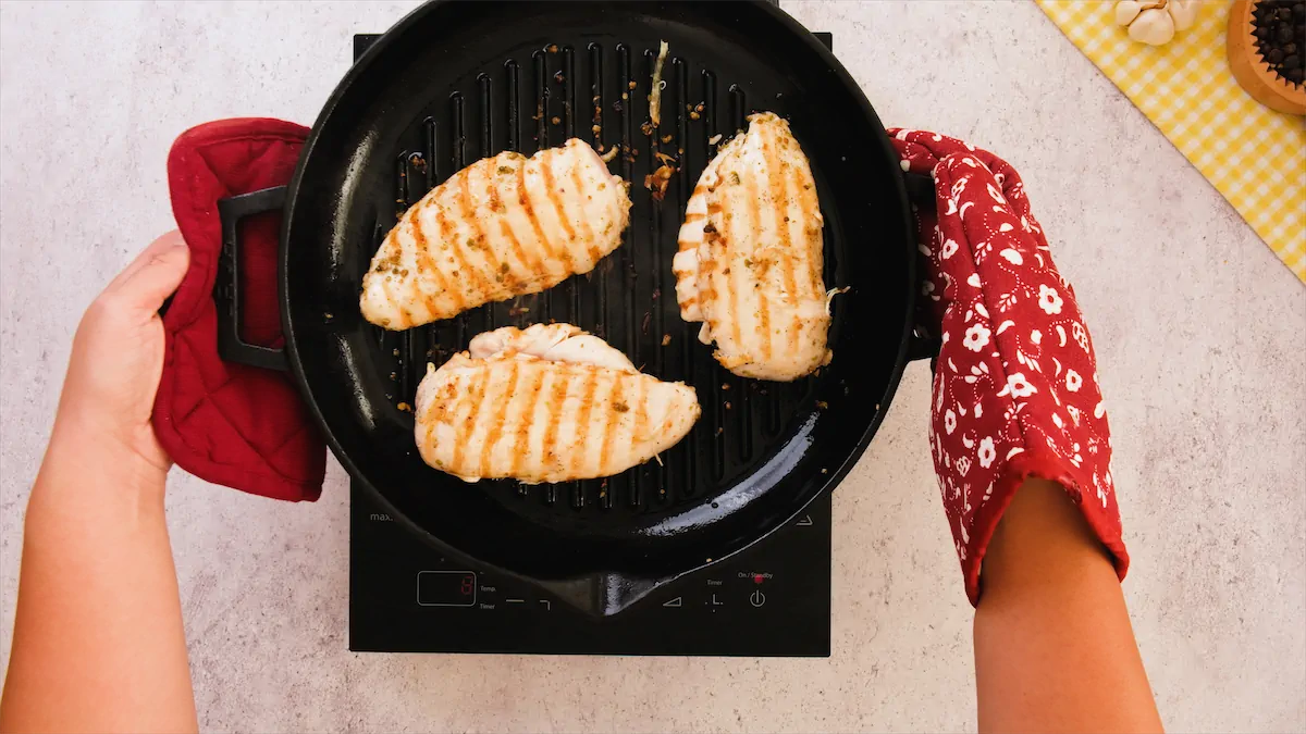 Removing the pan-seared chicken with golden marks from the induction top using mittens.