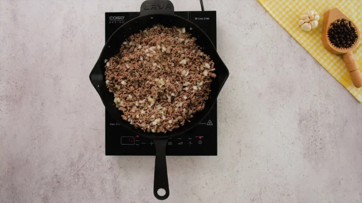 Ground beef cooking with aromatics in a cast iron skillet.