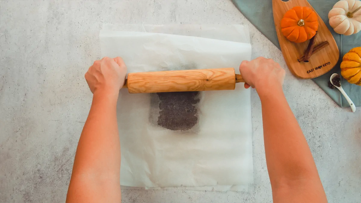Two hands are rolling out the cookie dough between two sheets of parchment paper with a rolling pin.