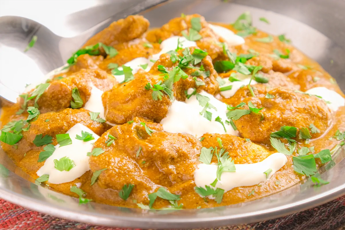 A serving dish containing low-carb Indian butter chicken, beautifully garnished with green herbs.