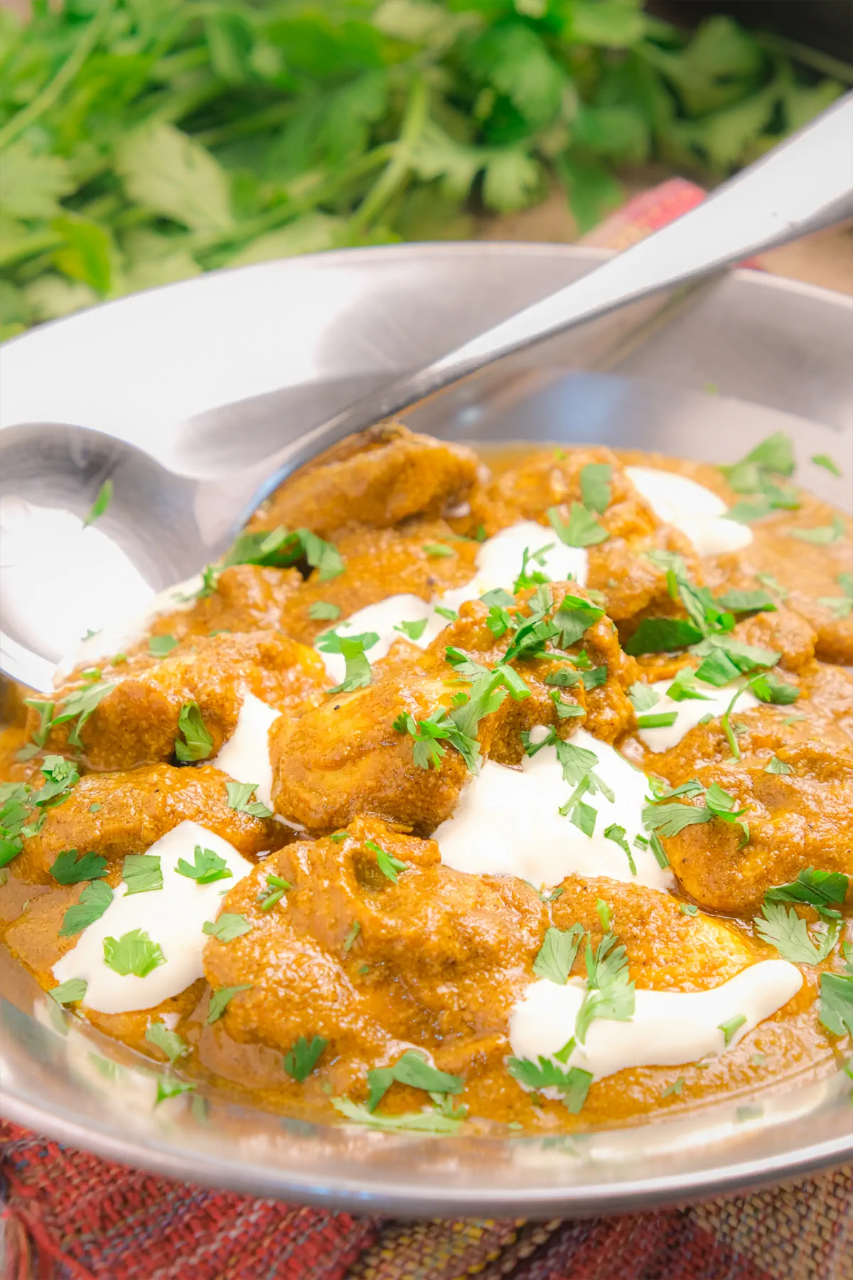 Keto Indian butter chicken, garnished with green herbs, served in a dish and a serving spoon.