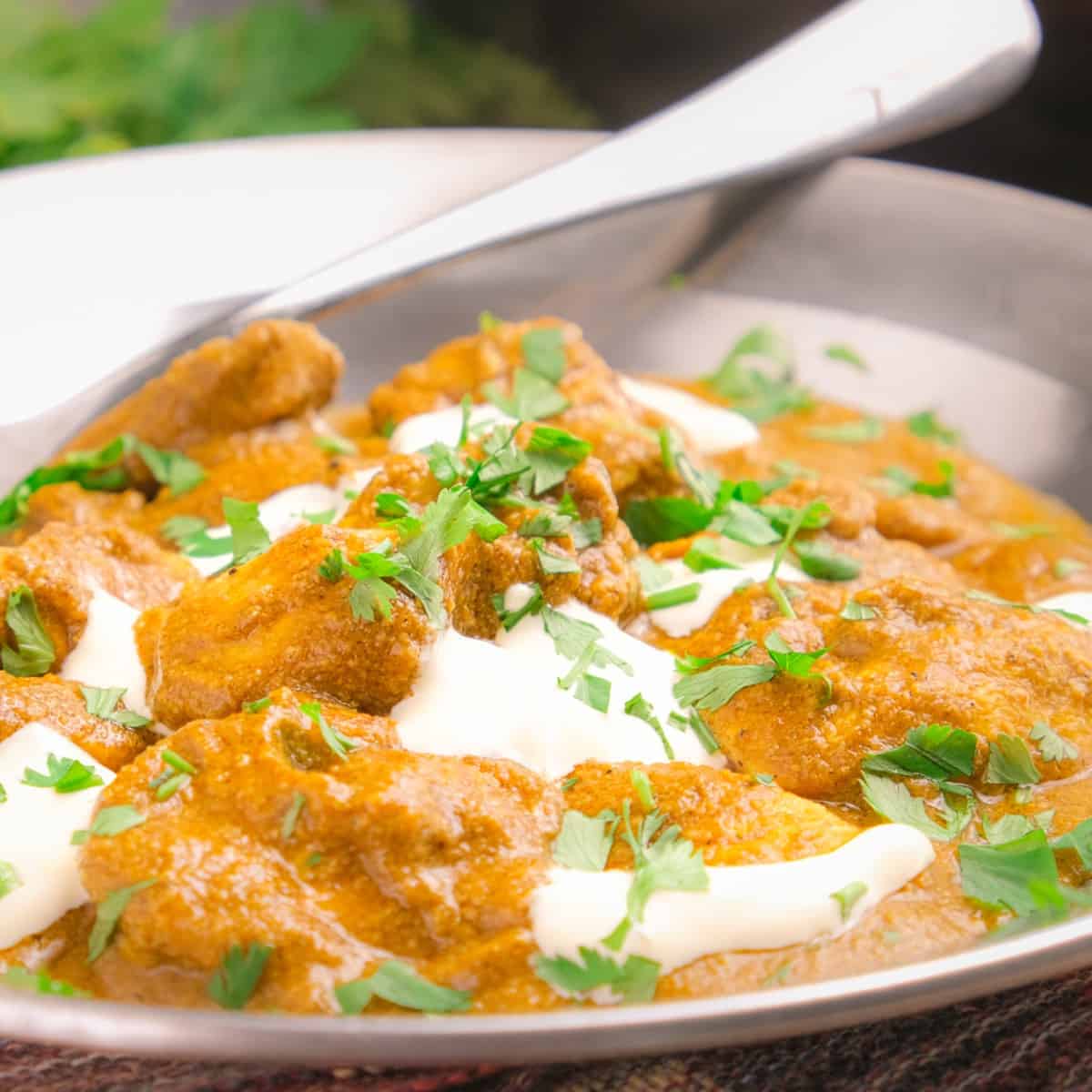 Keto Indian butter chicken garnished with green herbs in a serving dish.