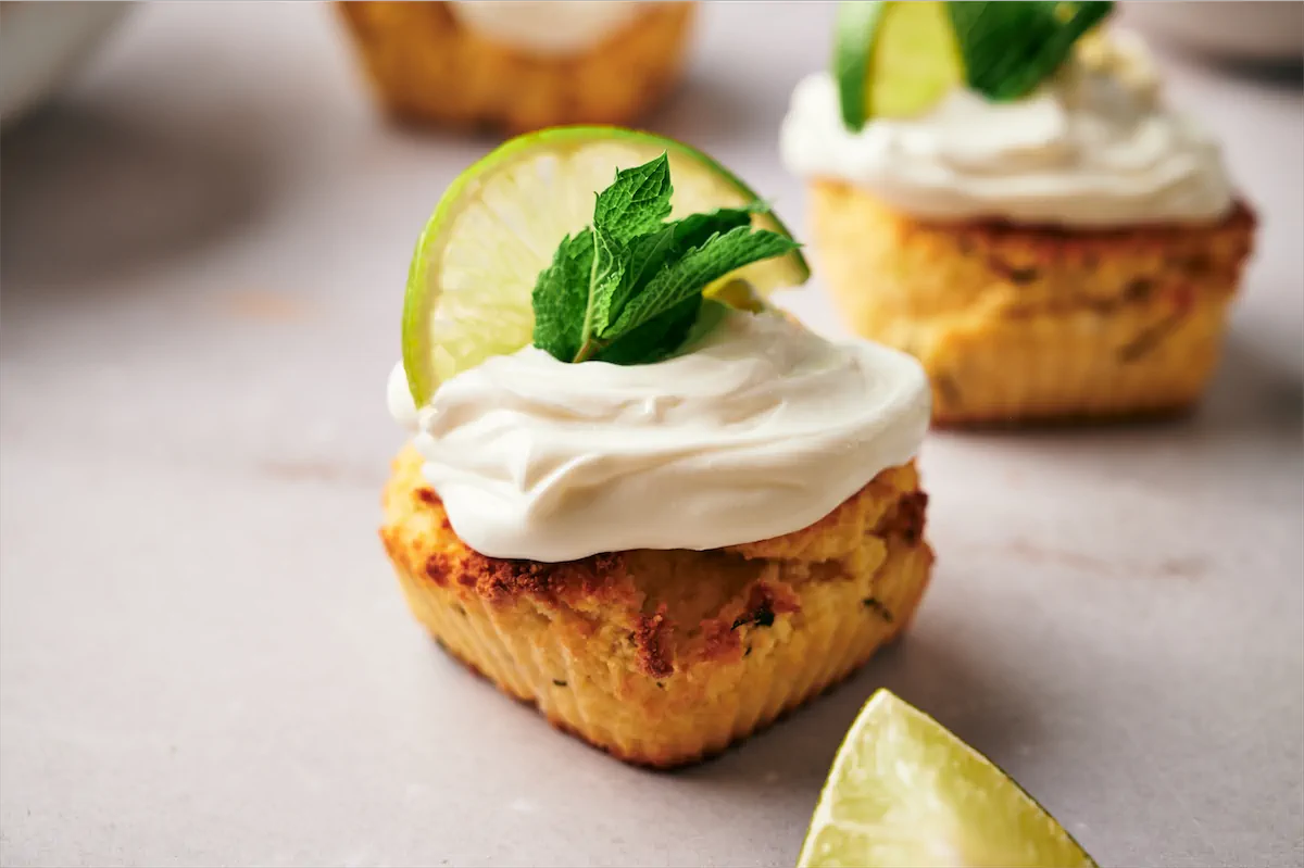Homemade keto mojito cupcakes topped with a cream cheese frosting, a lemon wedge, and mint leaves.