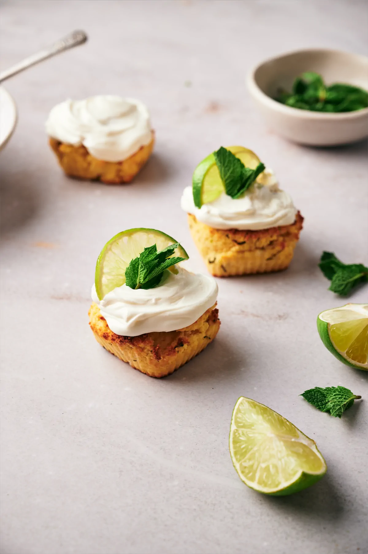 Sugar-free keto mojito cupcakes topped with cream cheese frosting and two are garnished with a lemon wedge and mint leaves.