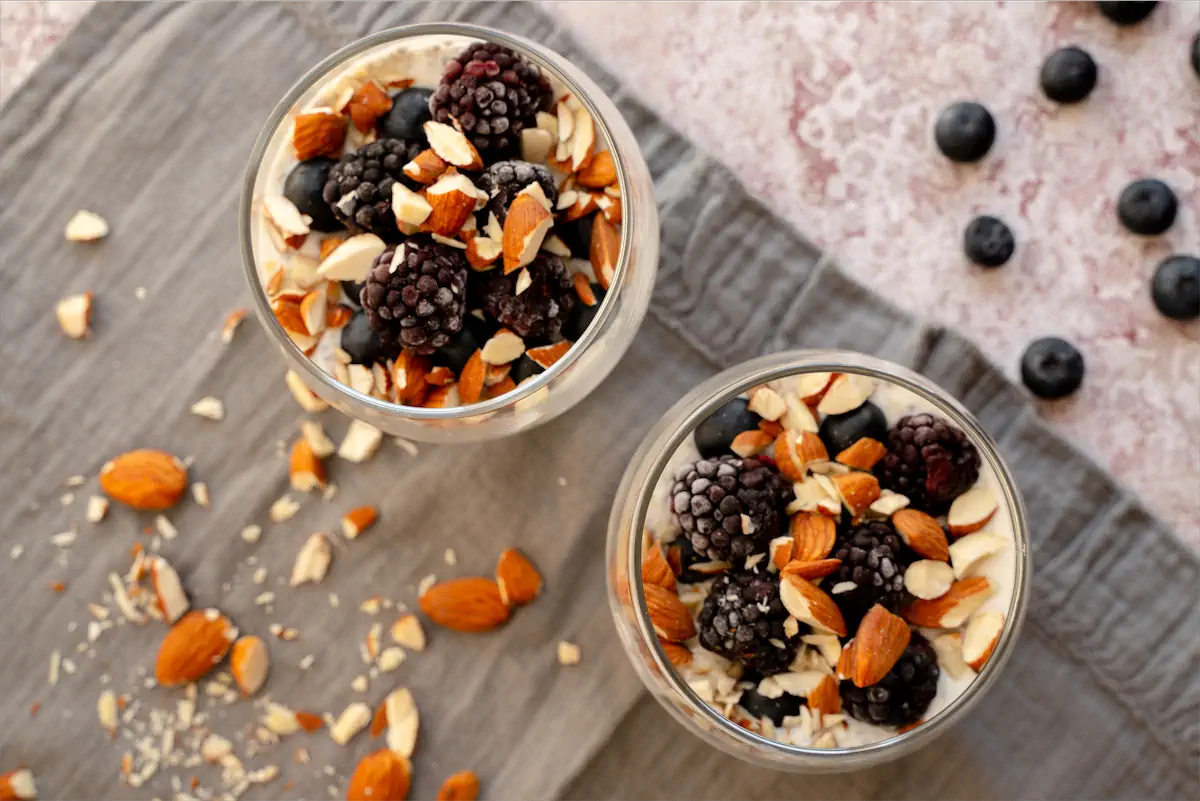 Low-carb overnight oats in yogurt and almond milk, topped with nuts and fresh berries in glass jars.