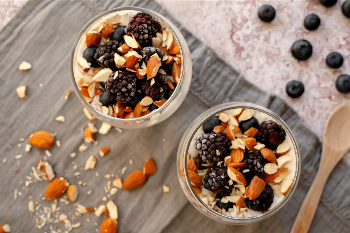 Homemade overnight oats in yogurt and almond milk, topped with nuts and fresh berries in glass jars.