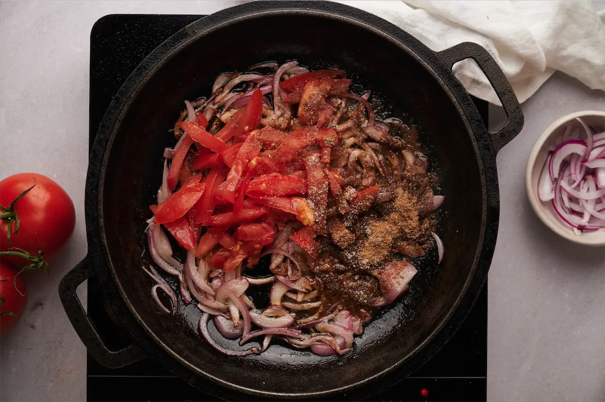 Cooking onions and tomatoes with spices in a cast iron skillet.