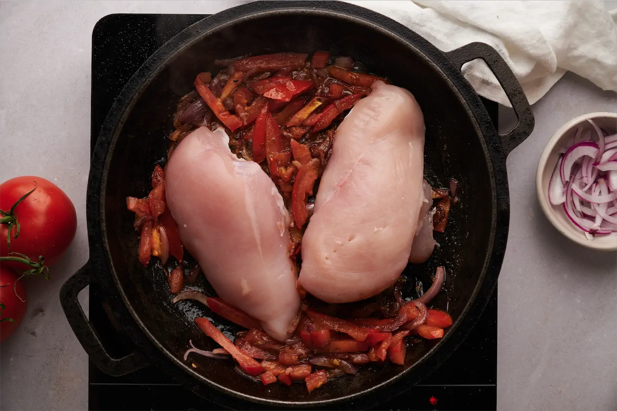Adding the skinless chicken breast to the cast iron skillet with the tomatoes.