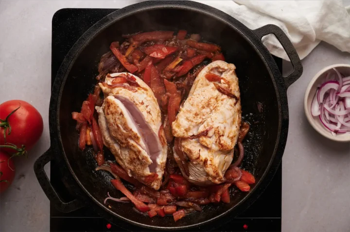 Cooking the chicken breast with sautéed onion, tomato and spices in a cast iron skillet.