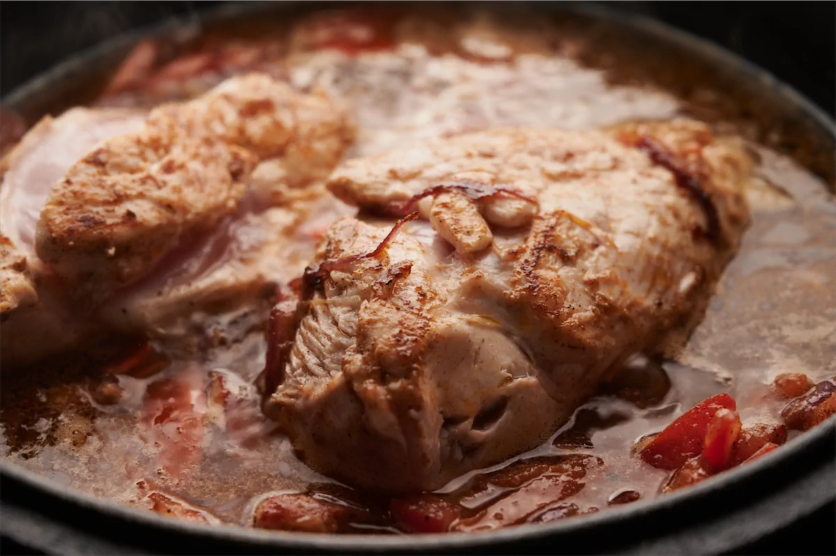Adding water to the chicken filet cooking with tomato based sauce in a cast iron skillet.