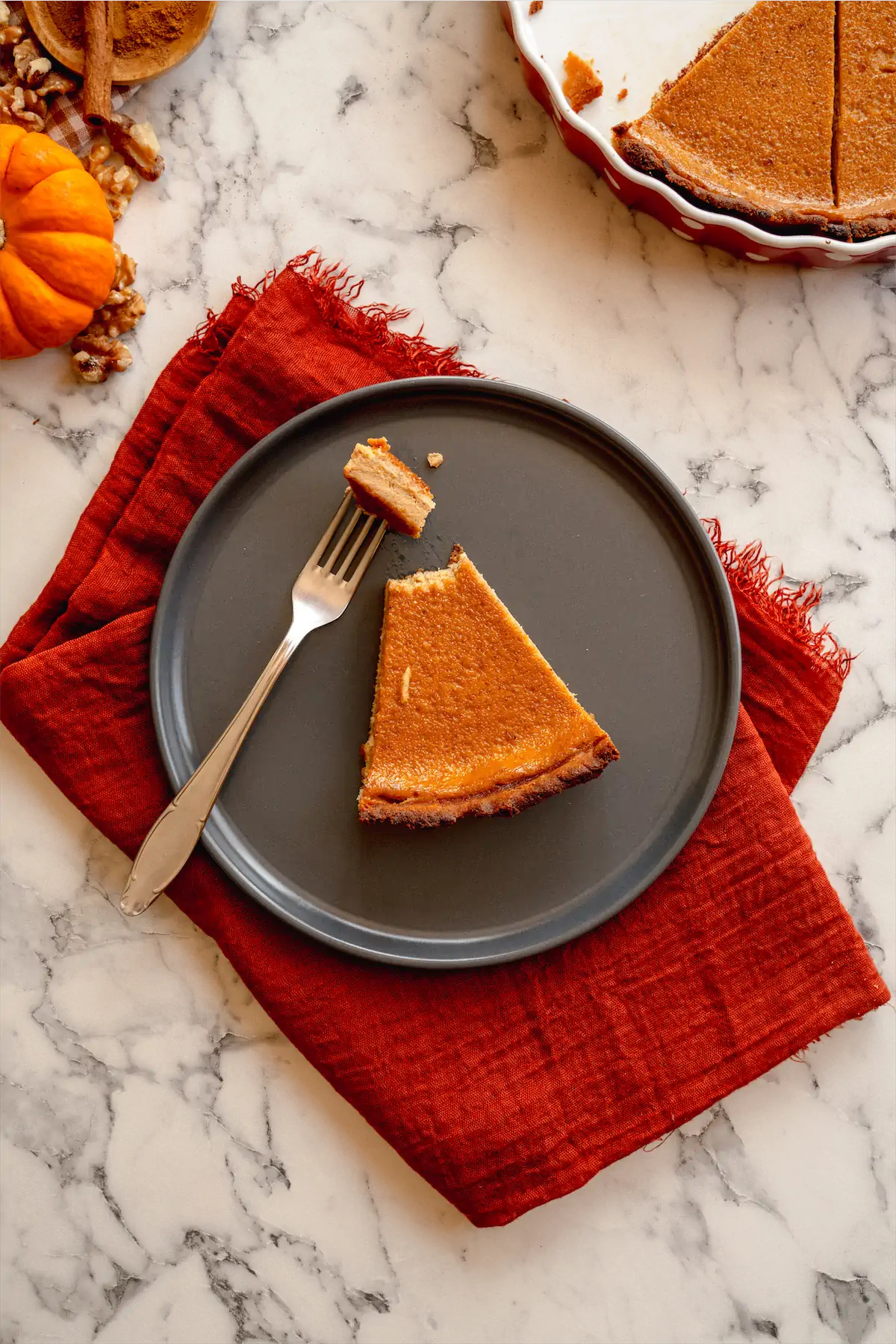 A slice of keto pumpkin pie served on a plate, with a morsel of pie on the fork.