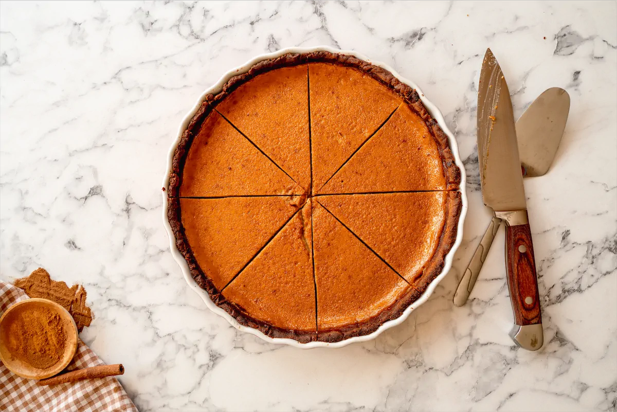 Sliced keto pumpkin pie in a pie dish with a knife and ready to be served with a pie server.