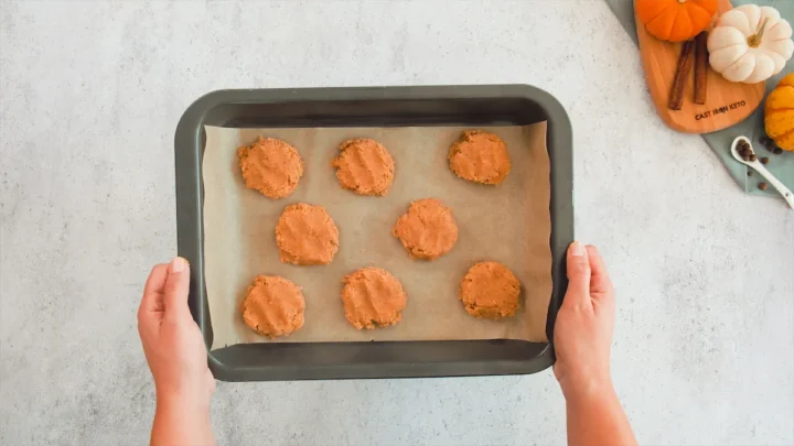 Two hands holding the baking sheet with ready-to-bake pumpkin spice cookies.