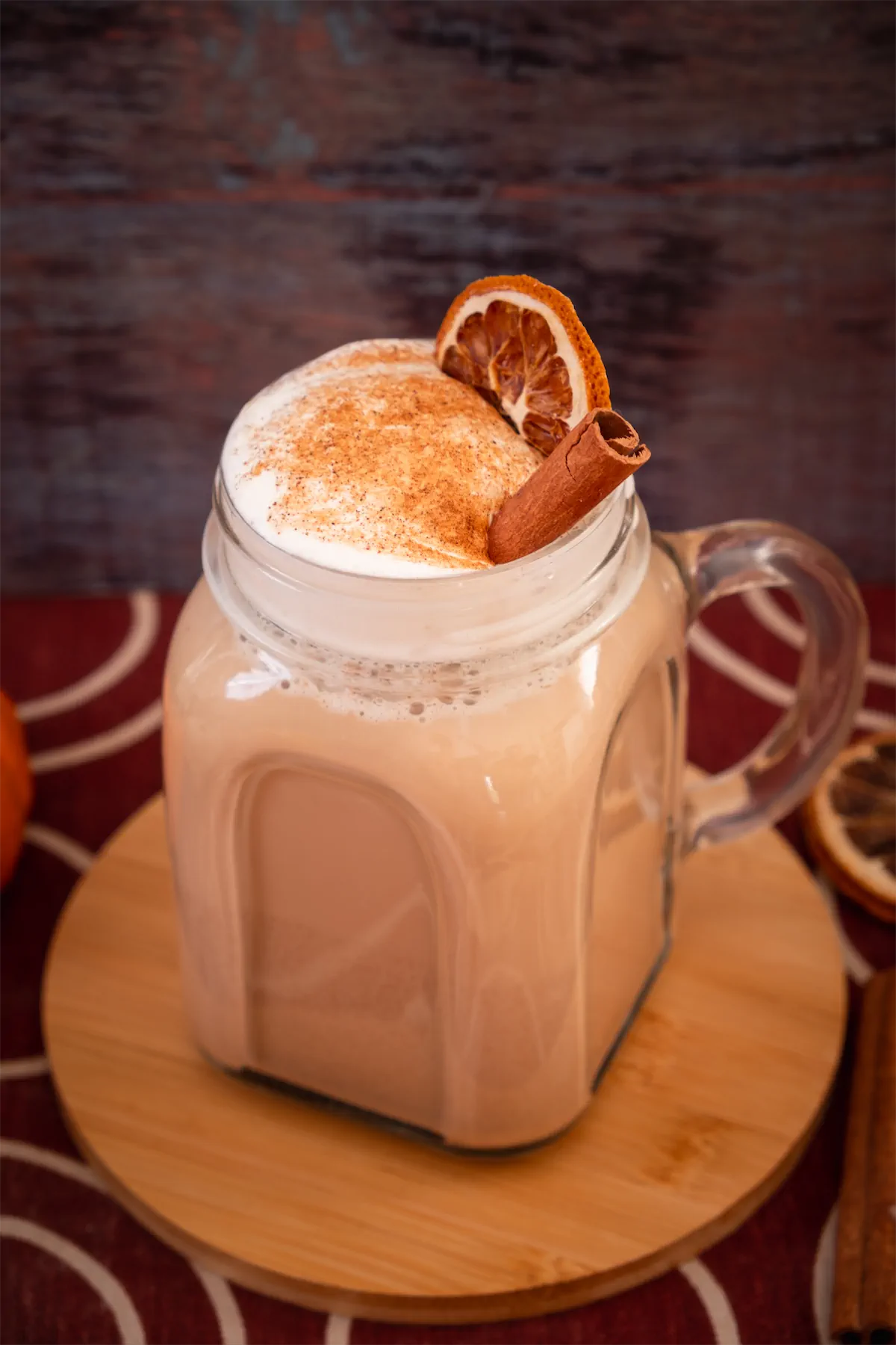 Homemade pumpkin spice latte in a mason jar with whipped cream, pumpkin spice, dried orange slice, and a cinnamon stick.