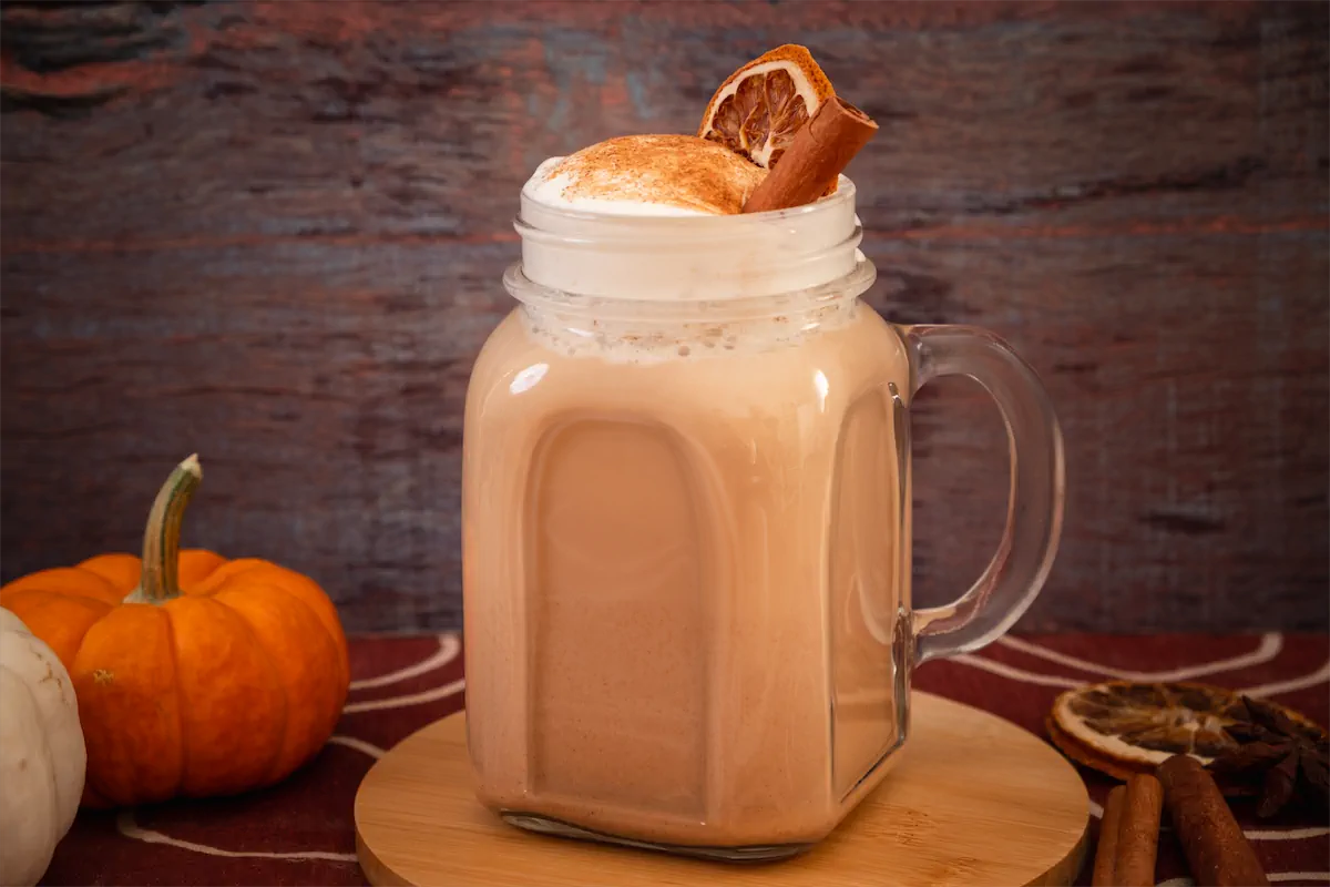 Keto pumpkin spice latte in a mason jar finished with whipped cream, pumpkin spice, dried orange slice, and a cinnamon stick.
