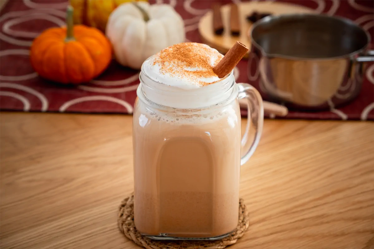 Homemade pumpkin spice latte recipe with almond milk served in a mason jar with a dollop of whipped cream, a dash of pumpkin spice and a cinnamon stick.