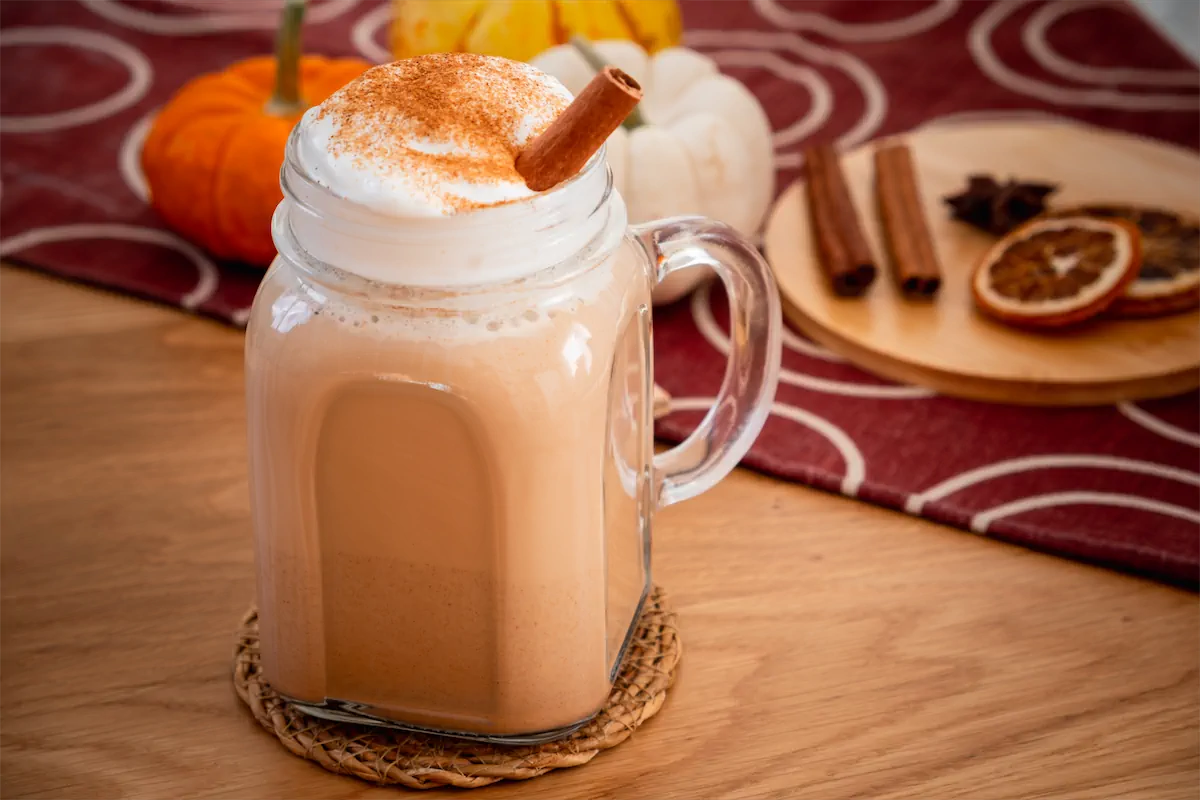 Homemade pumpkin spice latte recipe with almond milk served in a mason jar with a dollop of whipped cream and a dash of pumpkin spice.