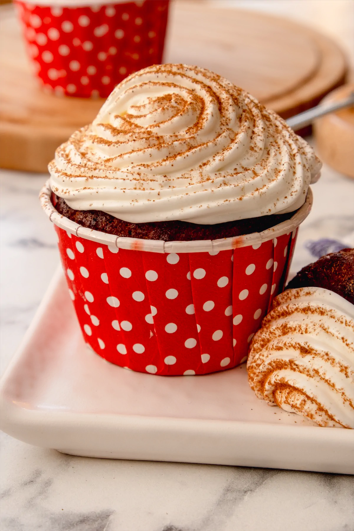 A pumpkin spice cupcake topped with whipped cream and a sprinkle of pumpkin spice.