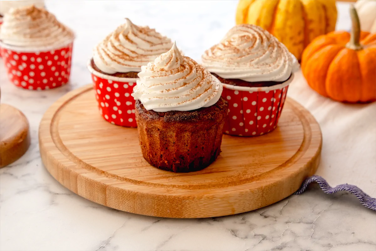 A sugar-free keto pumpkin spice latte cupcake, topped with whipped cream and pumpkin spice served on a round wooden board.