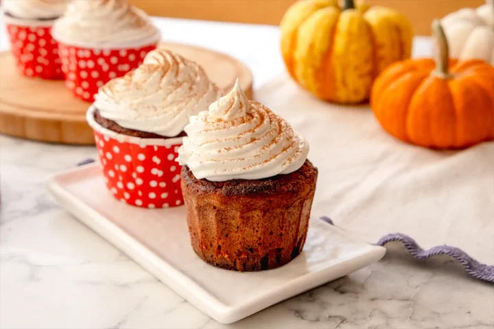 Pumpkin spice latte keto cupcake with whipped cream and a dash of pumpkin spice presented on a white plate.