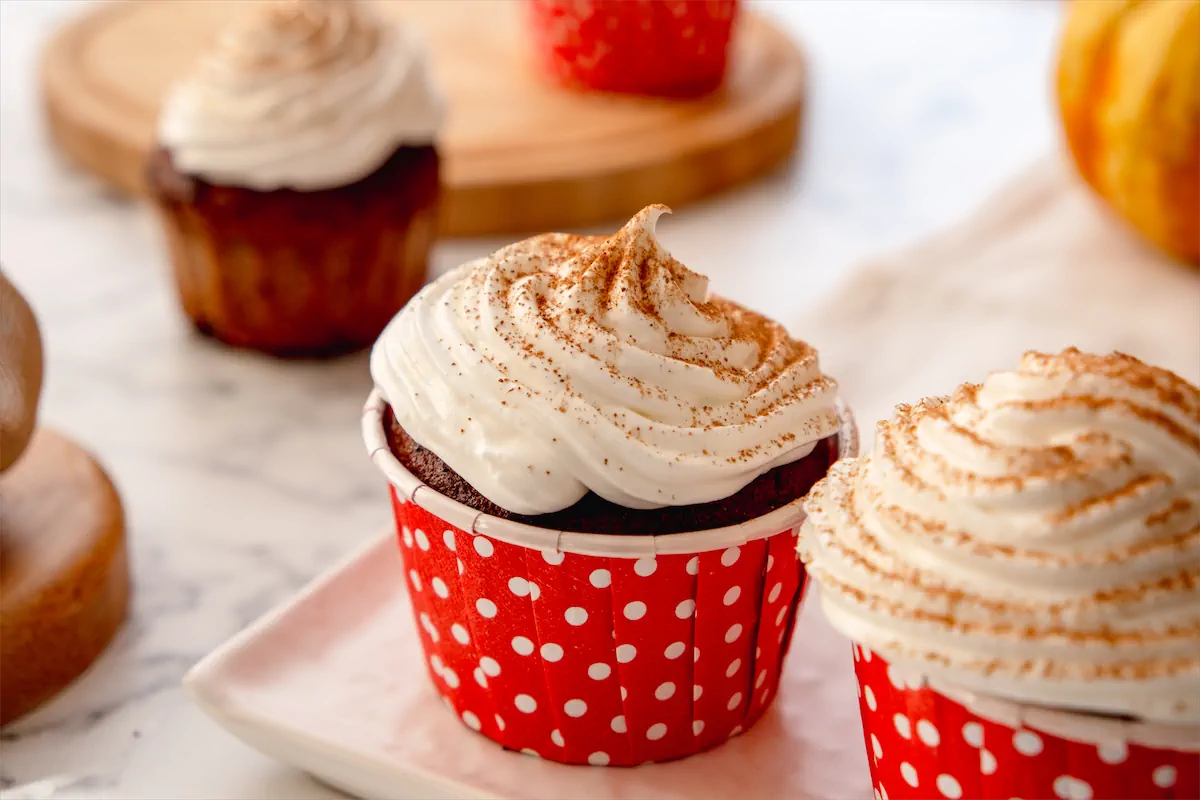 Keto pumpkin spice latte cupcakes topped with whipped cream and a sprinkle of pumpkin spice, presented in red polka dot cupcake paper molds.
