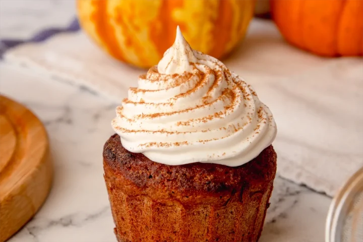 A closeup shot of a pumpkin spice latte cupcake topped with whipped cream and a sprinkle of pumpkin spice.