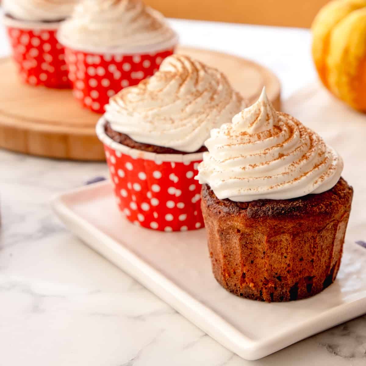 Keto pumpkin spice latte cupcakes topped with whipped cream and dash of pumpkin spice served on a white plate.