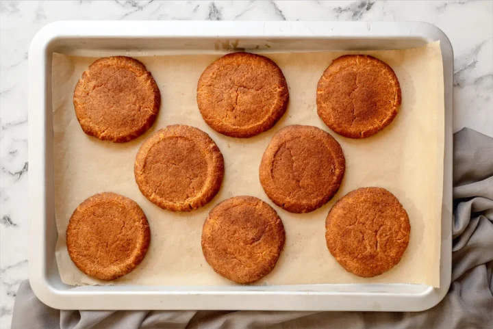 Freshly baked snickerdoodles on a white tray lined with parchment paper.