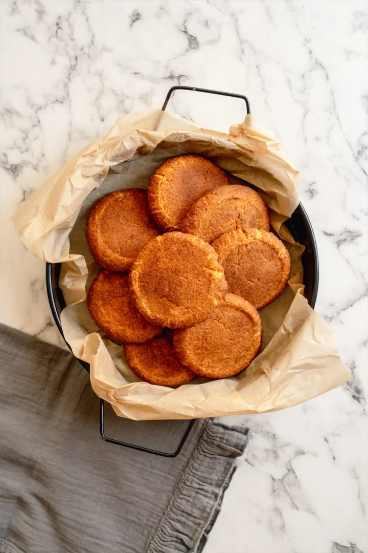 Freshly baked snickerdoodles arranged on a deep skillet lined with parchment paper.