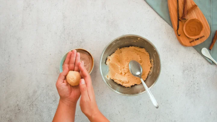 Scooping a spoonful of snickerdoodle dough from a bowl and rolling between their palms.
