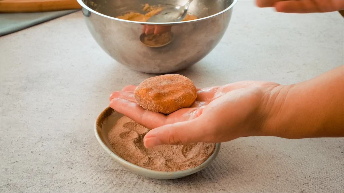 A hand holding a snickerdoodle dough coated in a mixture of granulated erythritol and ground cinnamon.