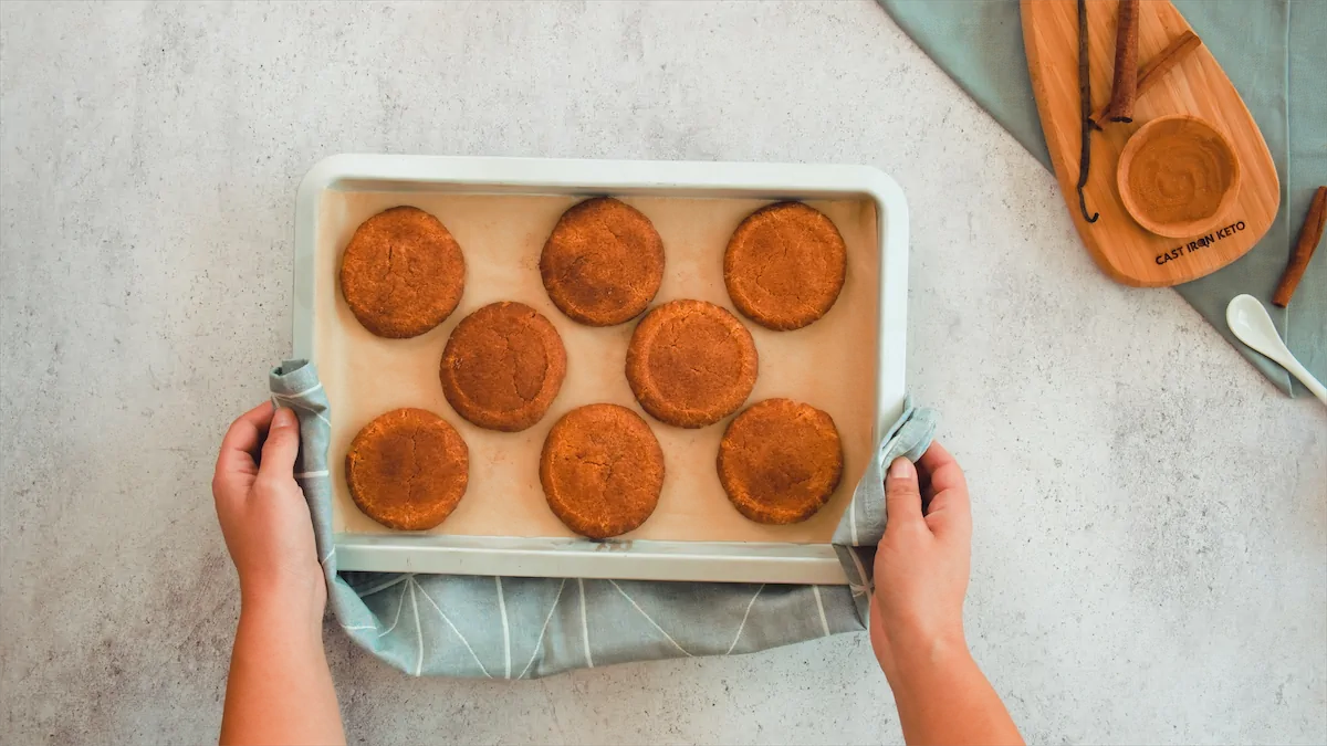 Two hands holding a hot tray of cooked snickerdoodles with a kitchen towel.