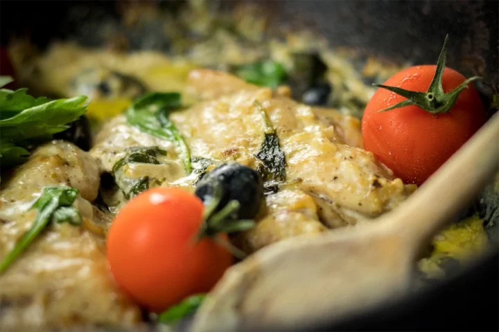 Homemade Tuscan chicken with a wooden spatula from a cast iron skillet.