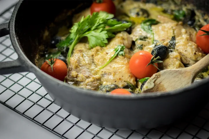 Keto Tuscan chicken ready to be served in a cast iron skillet with a wooden spatula.