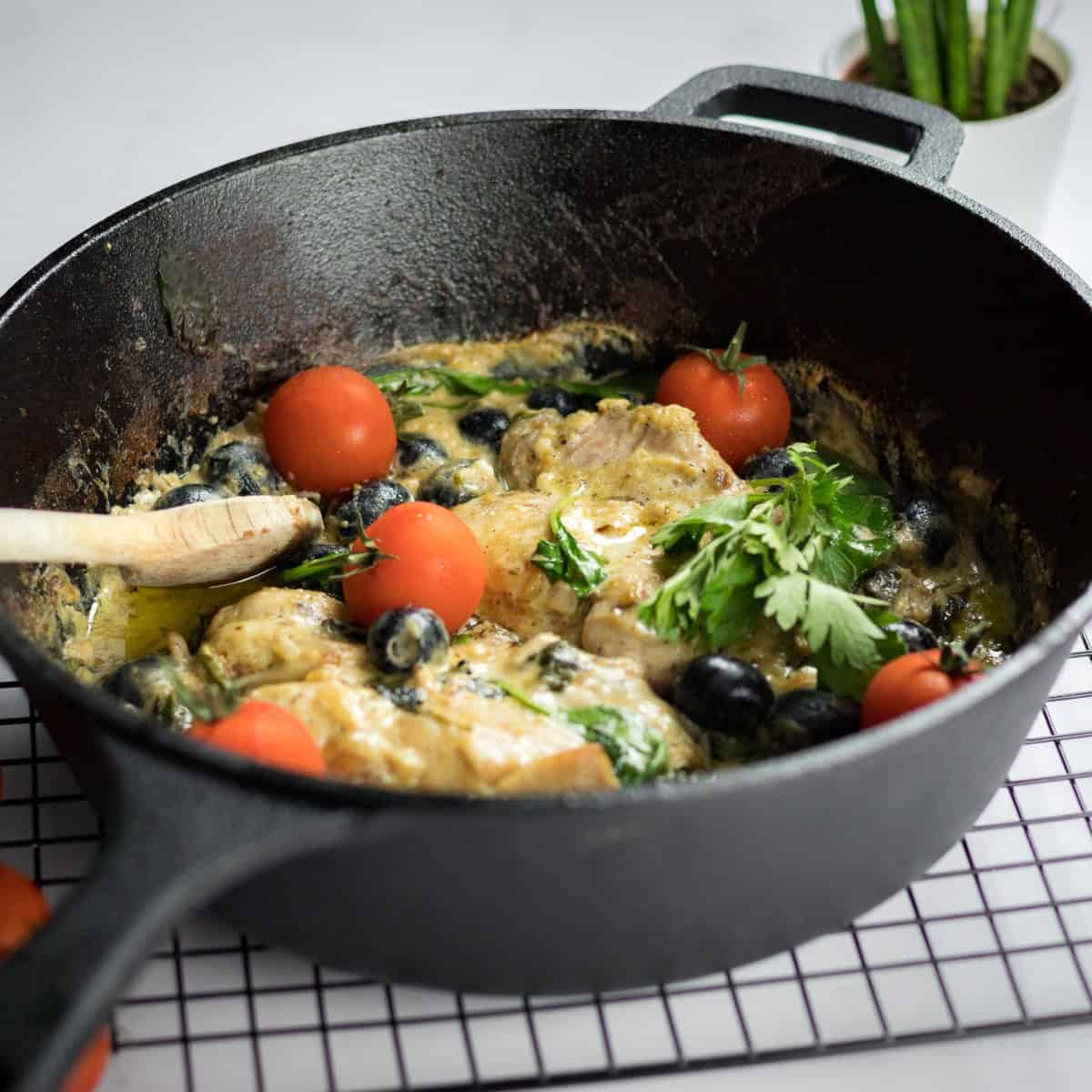 Creamy keto Tuscan chicken garnished with cherry tomatoes and fresh green herbs in a cast iron skillet.