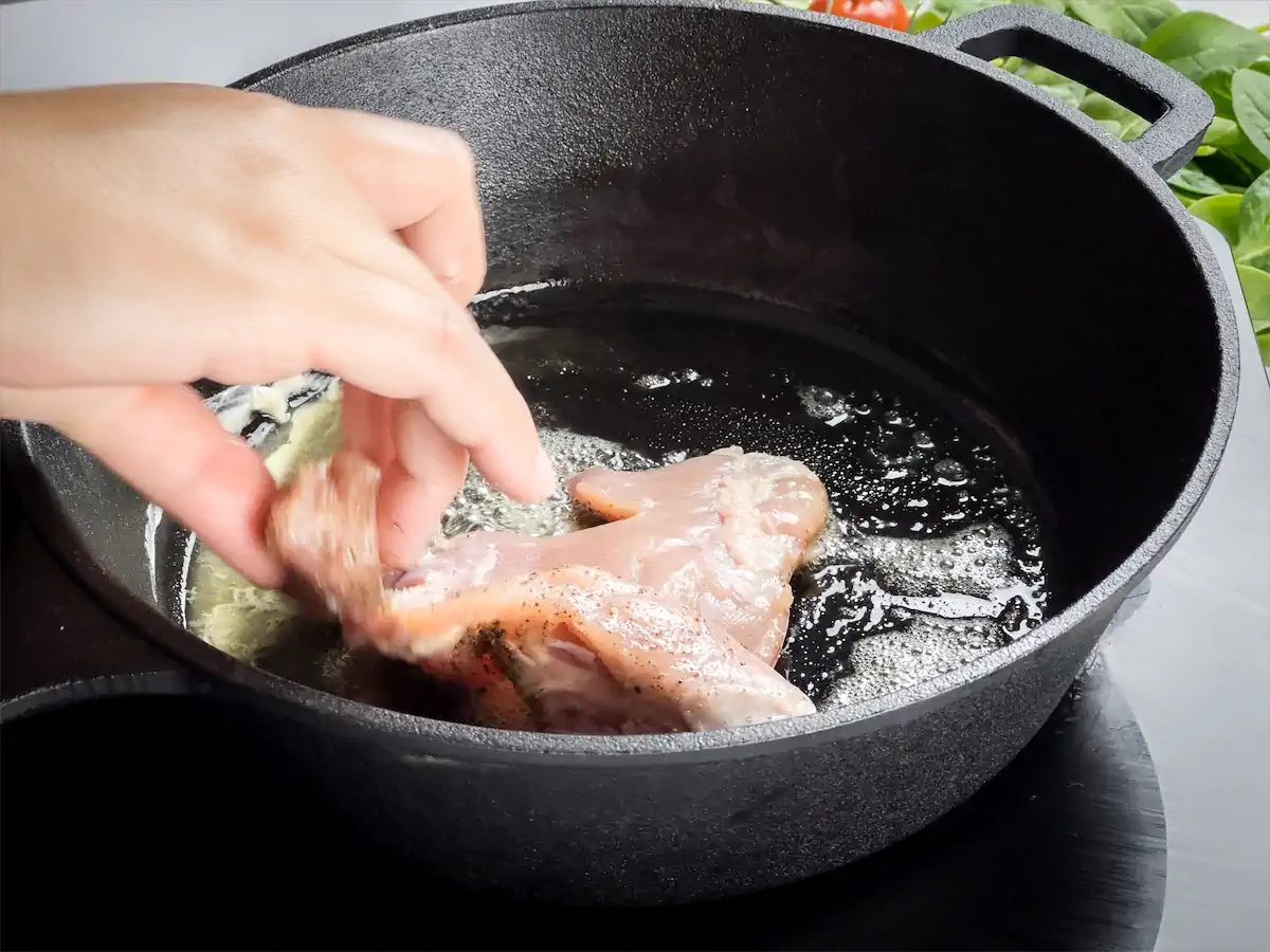 Adding skinless and boneless chicken to the cast iron skillet with melted butter.
