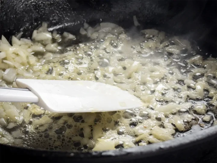 Sautéing diced onion in a cast iron skillet with butter.